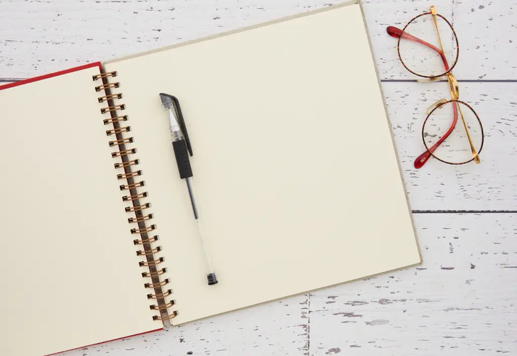 Sur une table lumineuse, des lunettes posées près d’un carnet ouvert et d’un stylo
